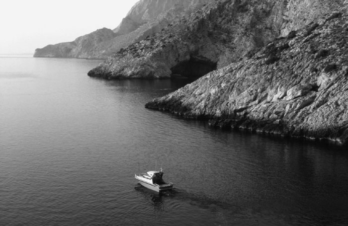 Black and white photo of Plate 1.1A. The west side of Youra, view from south. The entrance of a littoral cave is visible on the coast.